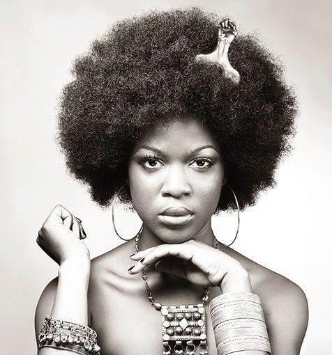 Dark skinned woman wearing an afro hairstyle. She has a "black-fist" style hair pic sticking up from her hair.